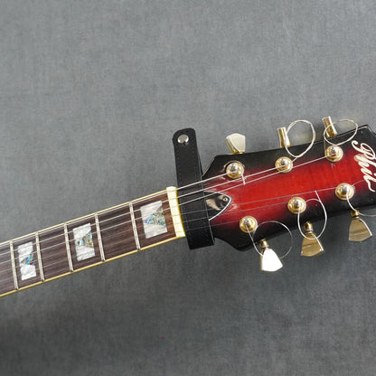 A close-up of a guitar headstock adapter from black smooth leather