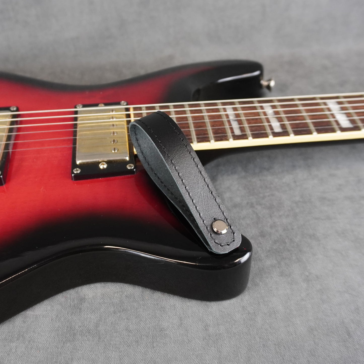 A close-up of an electric guitar with a black smooth leather guitar headstock adapter