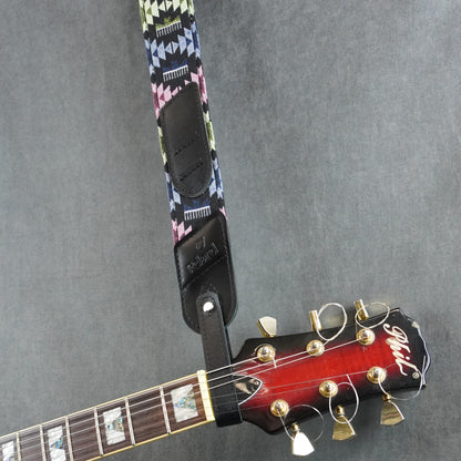 A guitar strap with a colorful fabric with black smooth leather headstock adapter