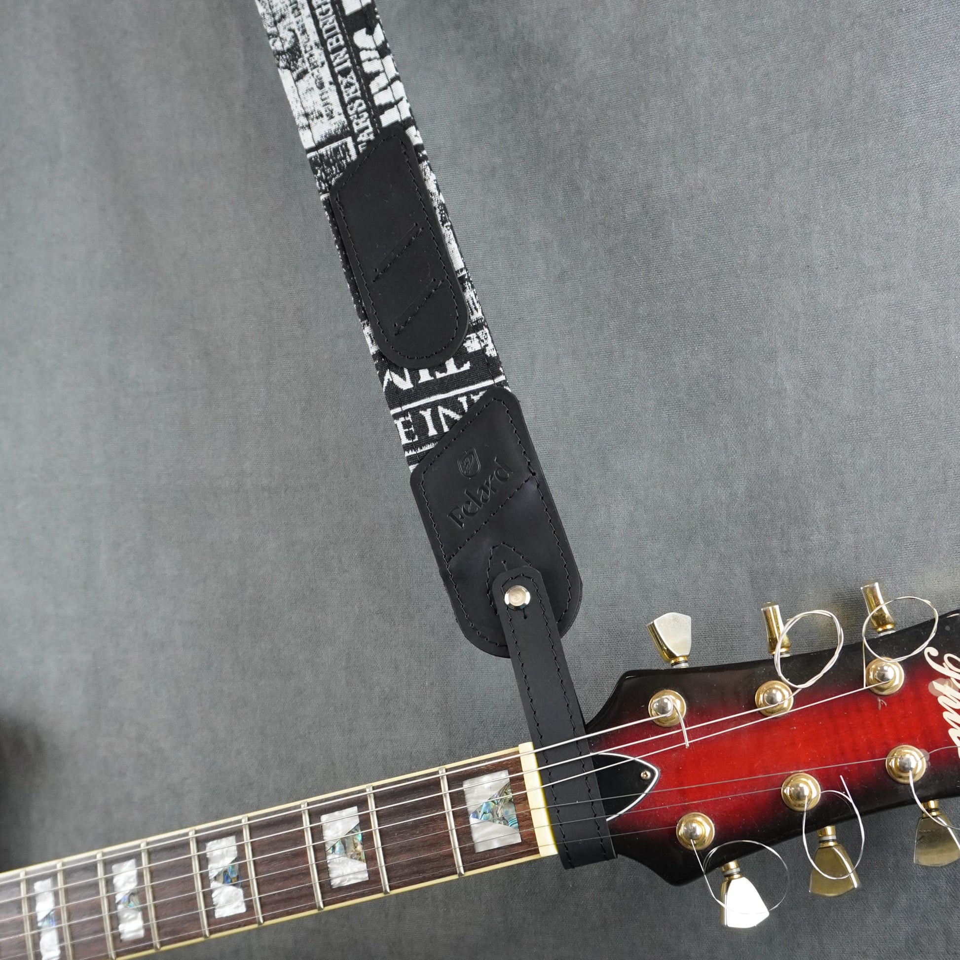 A guitar strap with black & white fabric with black matte leather headstock adapter