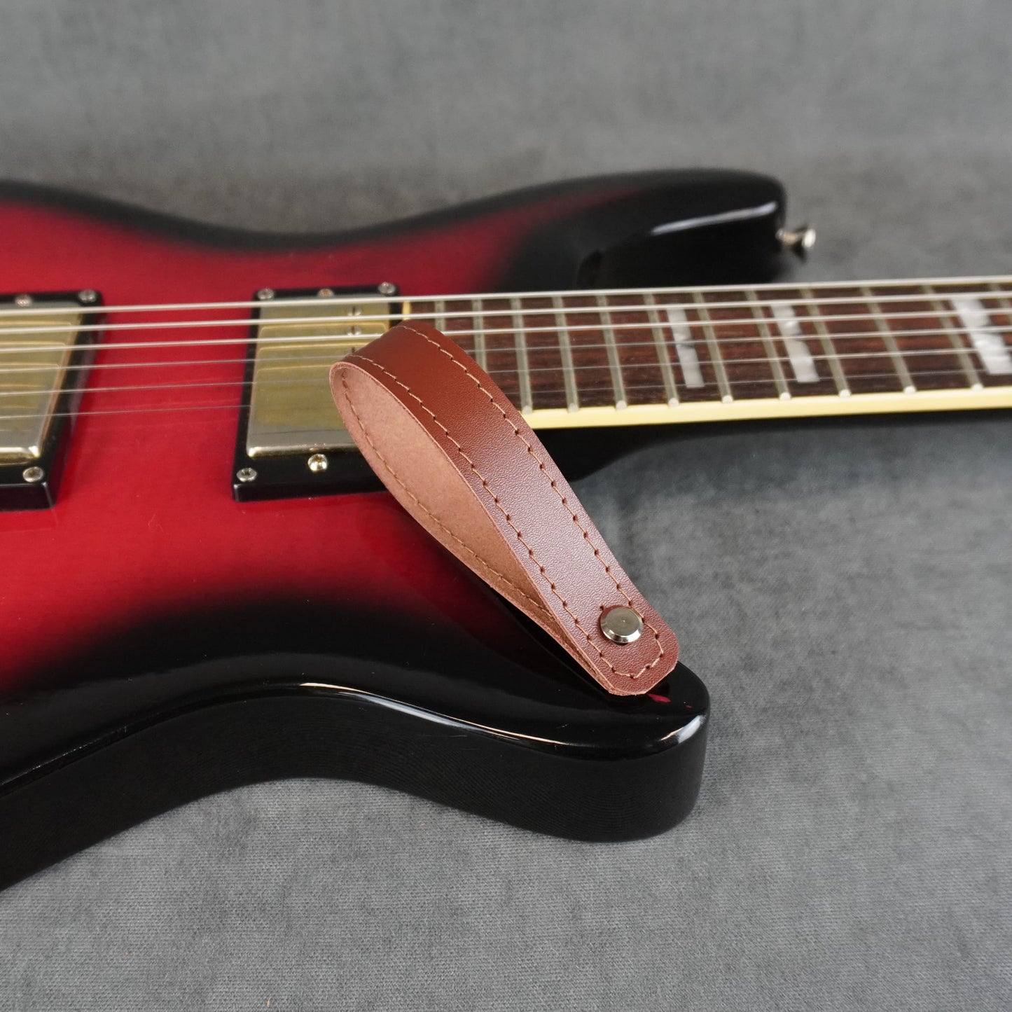 A close-up of an electric guitar with a cognac smooth leather guitar headstock adapter