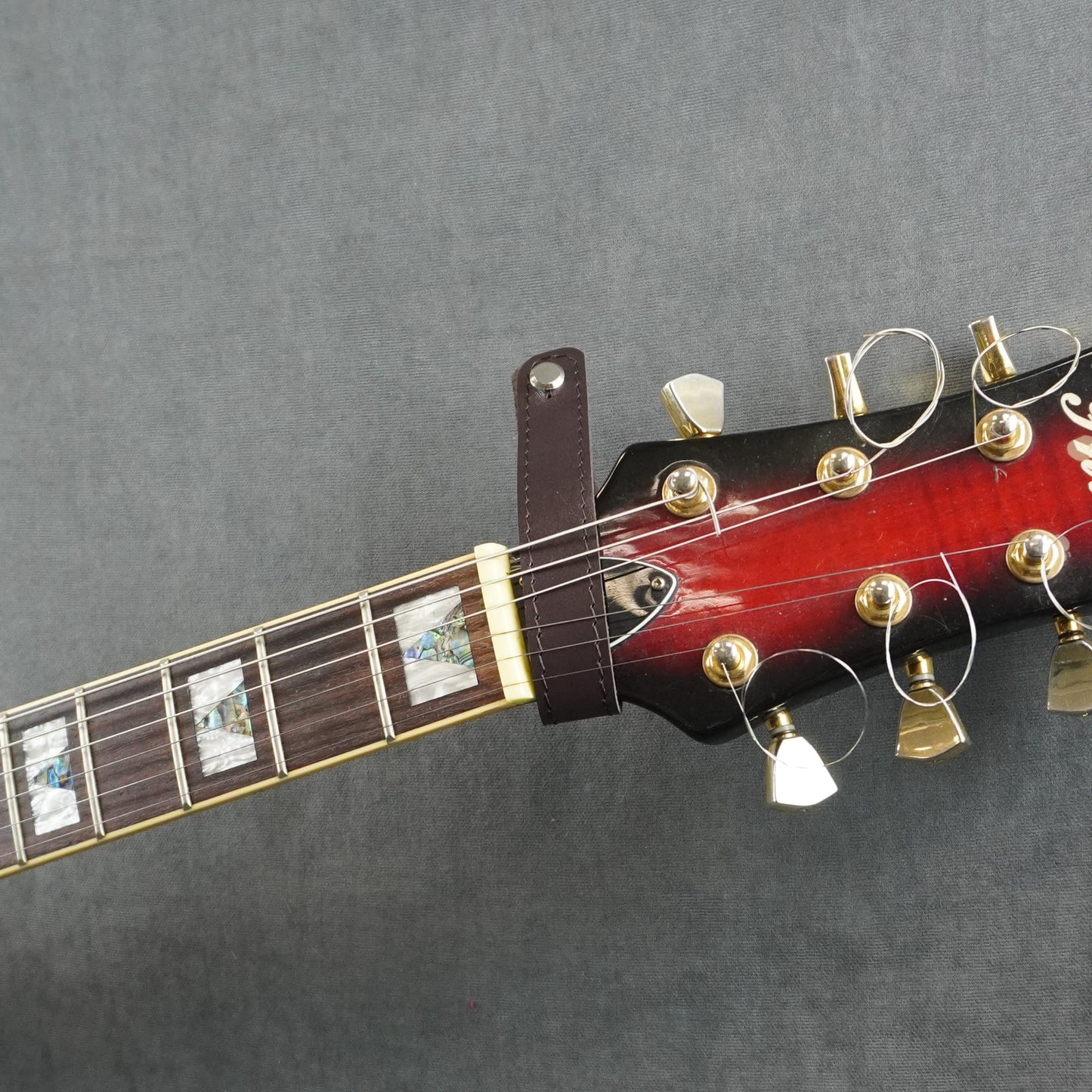 A close-up of a guitar headstock adapter from dark brown smooth leather