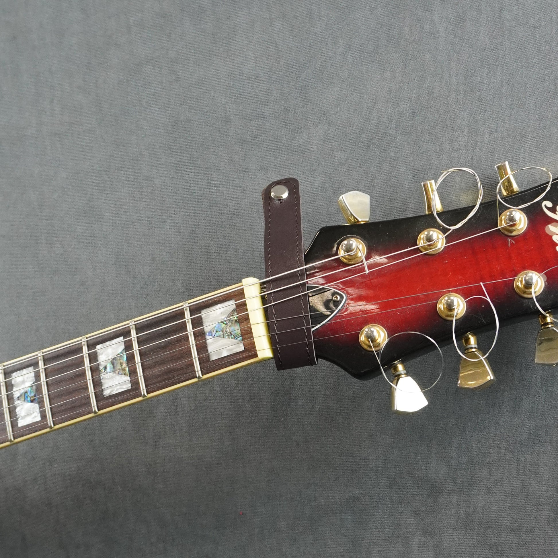 A close-up of a guitar headstock adapter from dark brown smooth leather