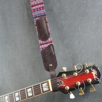 A guitar strap with a colorful striped fabric with dark brown smooth leather headstock adapter