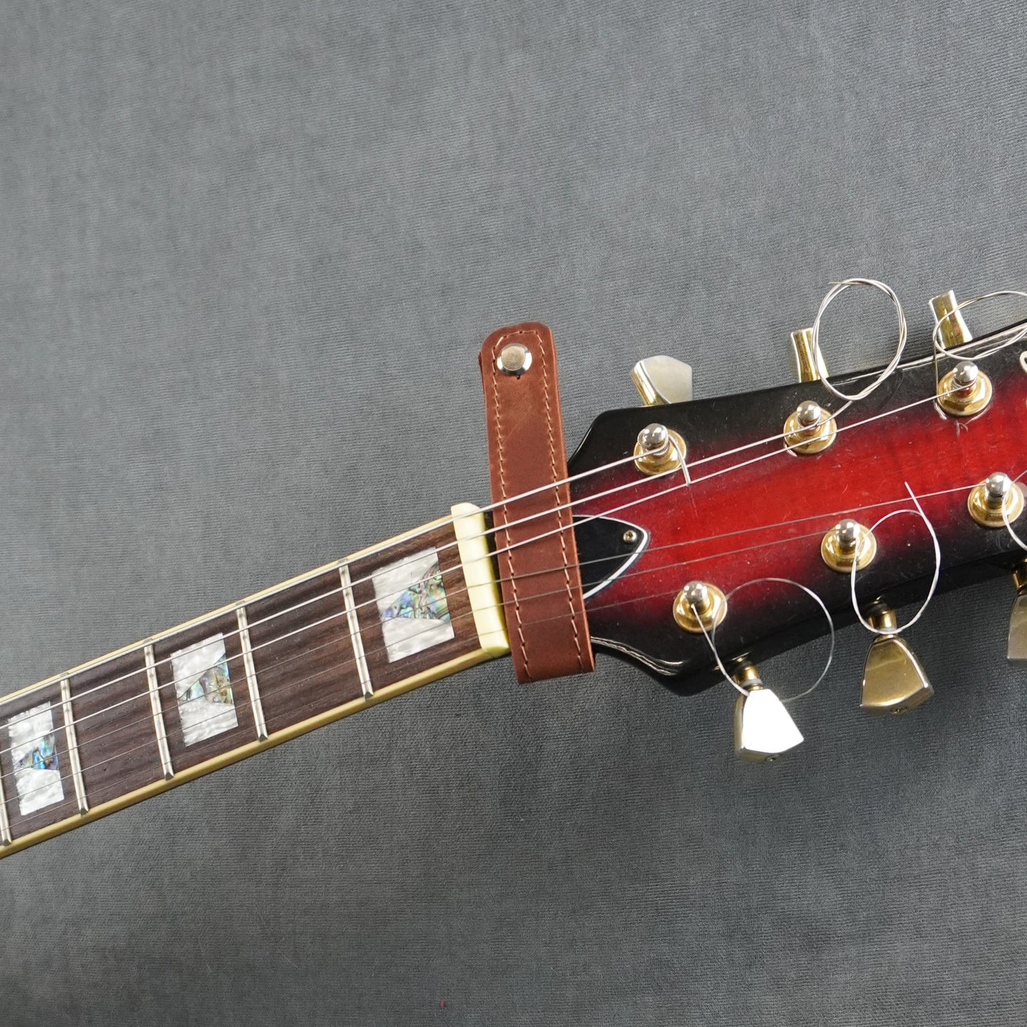 A close-up of a guitar headstock adapter from dark cognac matte leather