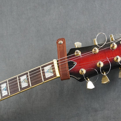 A close-up of a guitar headstock adapter from dark cognac matte leather