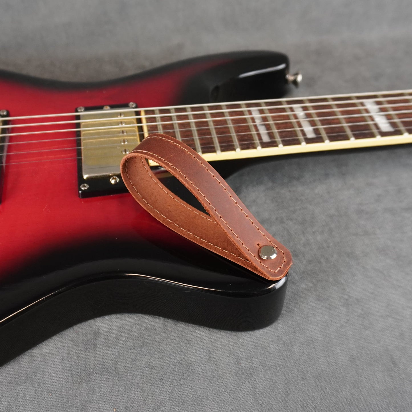 A close-up of an electric guitar with a dark cognac leather guitar headstock adapter