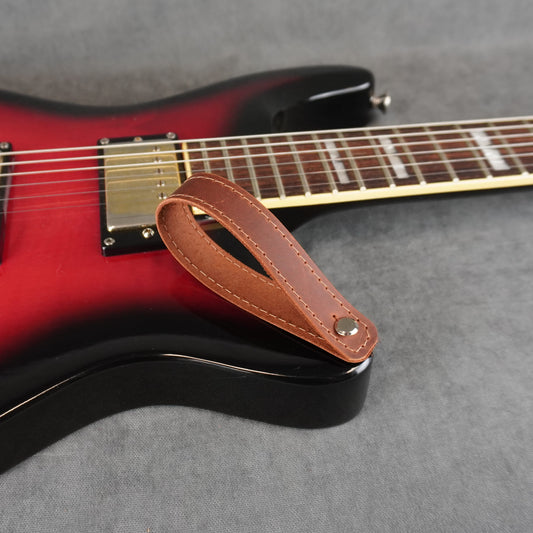 A close-up of an electric guitar with a dark cognac leather guitar headstock adapter