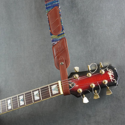 A guitar strap with a colorful striped fabric with cognac smooth leather headstock adapter