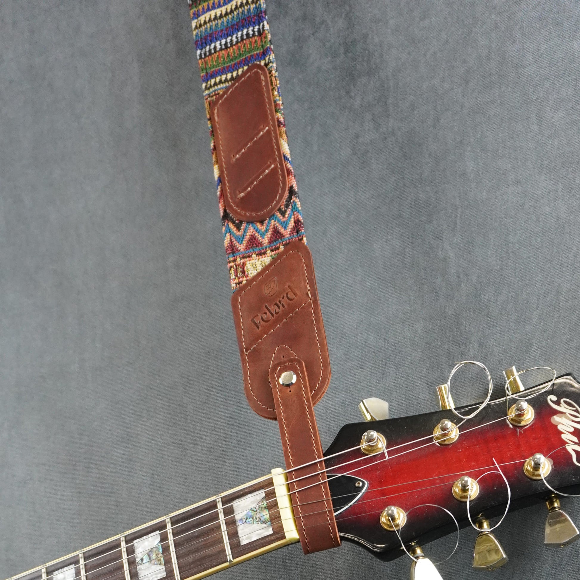 A guitar strap with a colorful striped fabric with dark cognac matte leather headstock adapter