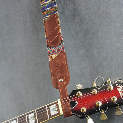 A guitar strap with a colorful striped fabric with dark cognac matte leather headstock adapter