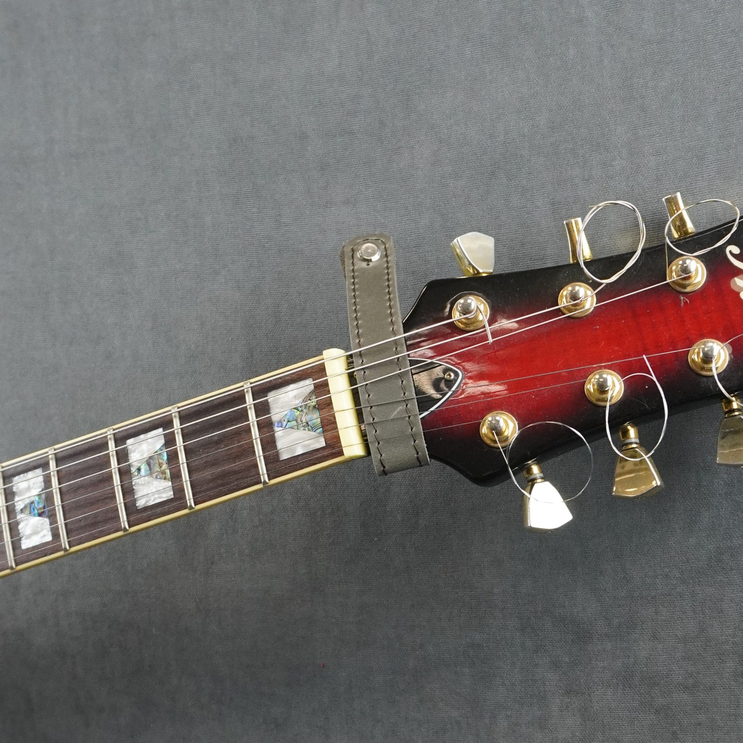 A close-up of a guitar headstock adapter from gray matte leather