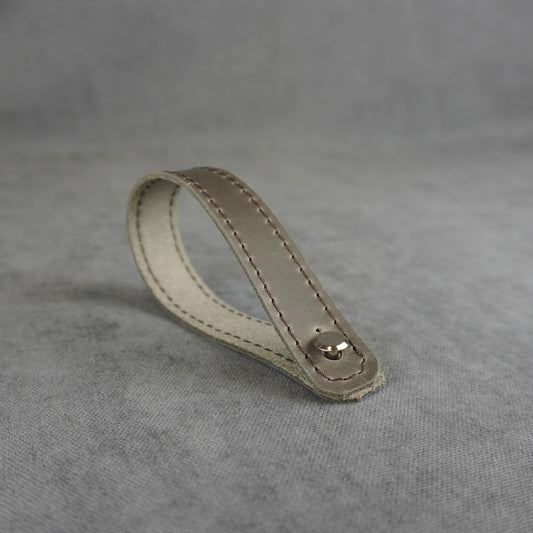 A gray matte leather strap headstock adapter with a single silver metal rivet, photographed on a textured gray background.