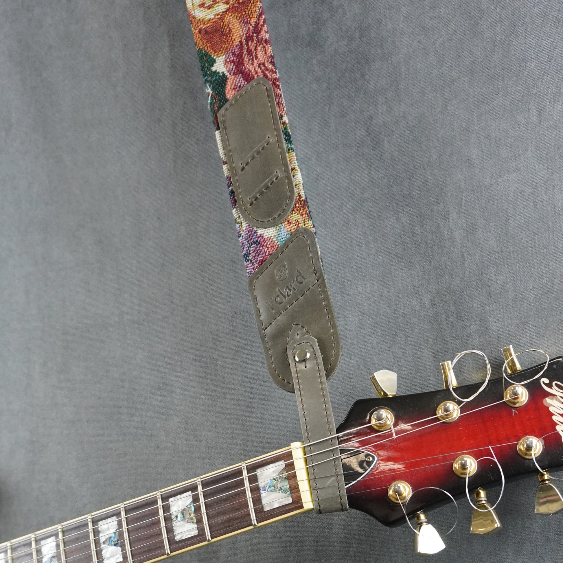 A guitar strap with a colorful striped fabric with gray matte leather headstock adapter
