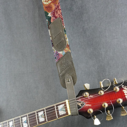 A guitar strap with a colorful striped fabric with gray matte leather headstock adapter