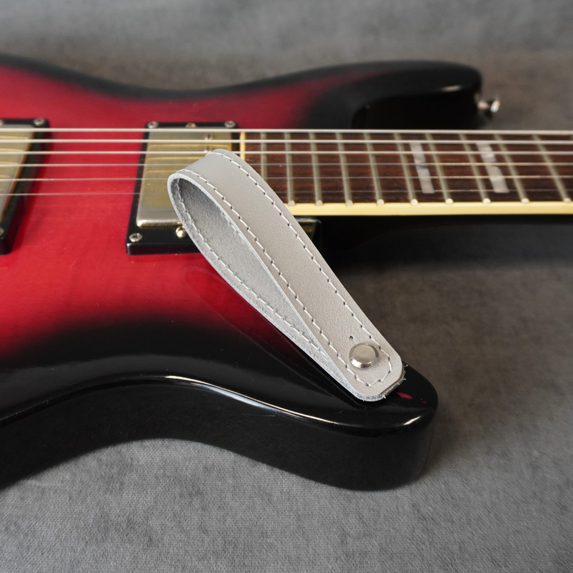 A close-up of an electric guitar with a gray smooth leather guitar headstock adapter