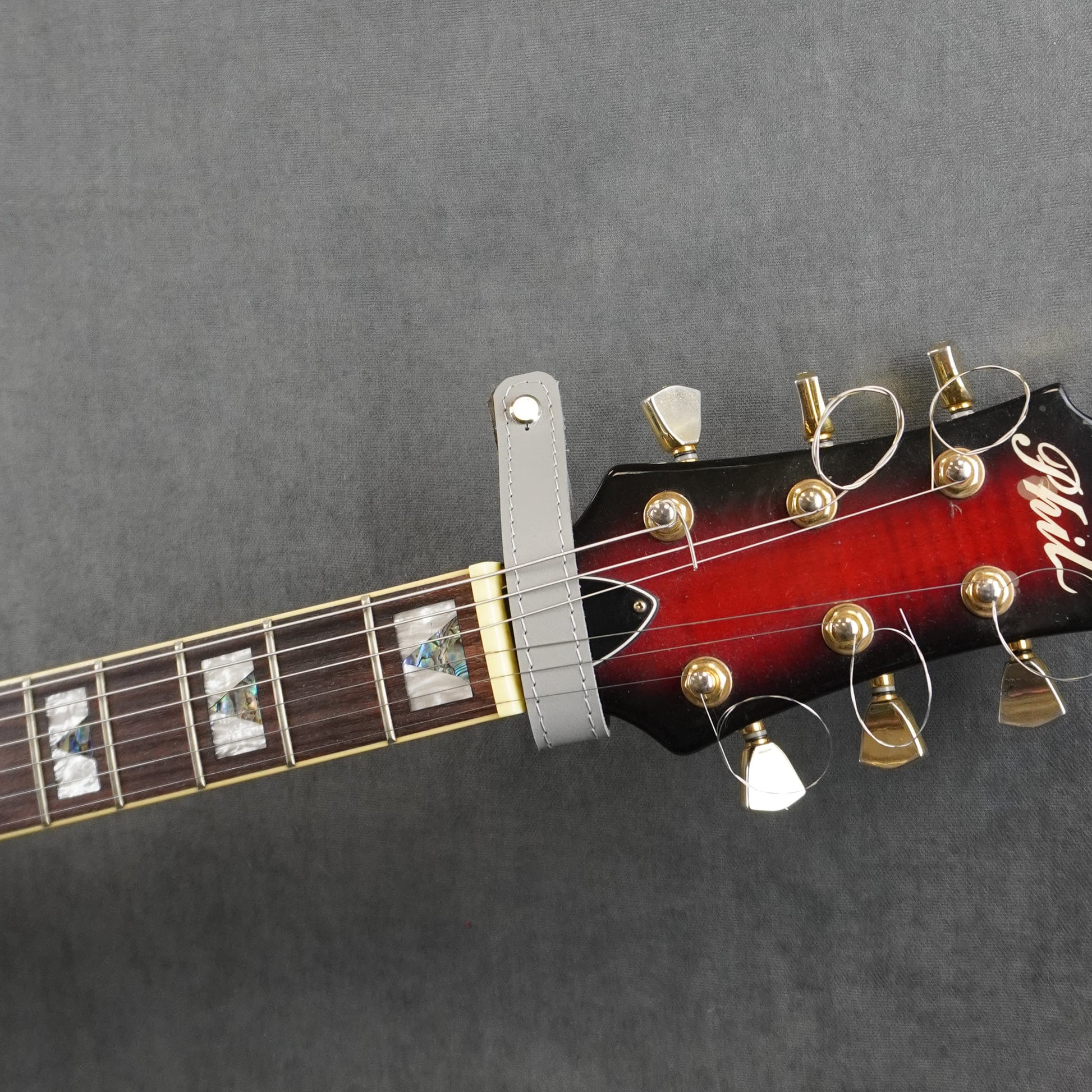 A close-up of a guitar headstock adapter from gray smooth leather