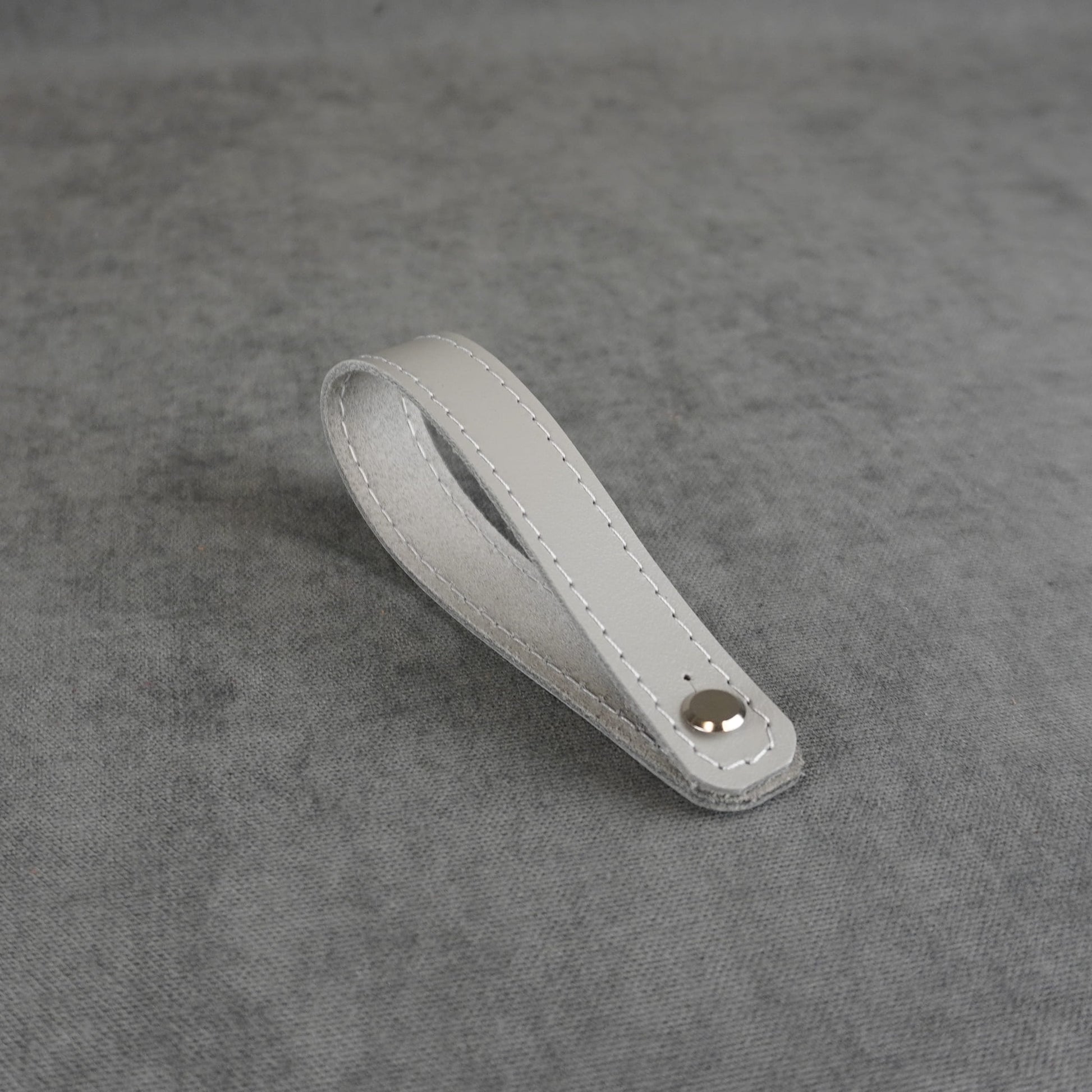 A gray smooth leather strap headstock adapter with a single silver metal rivet, photographed on a textured gray background.