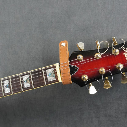 A close-up of a guitar headstock adapter from tan leather