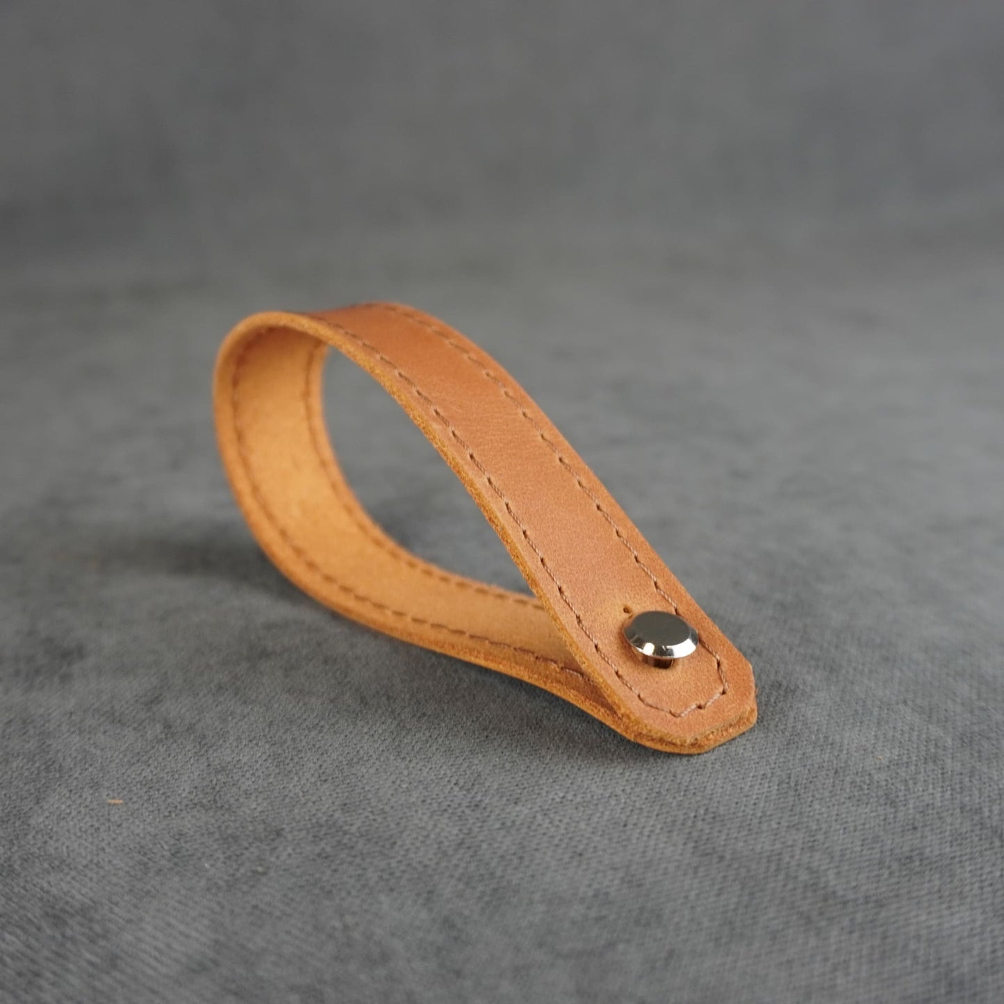 A light tan leather strap headstock adapter with a single silver metal rivet, photographed on a textured gray background.