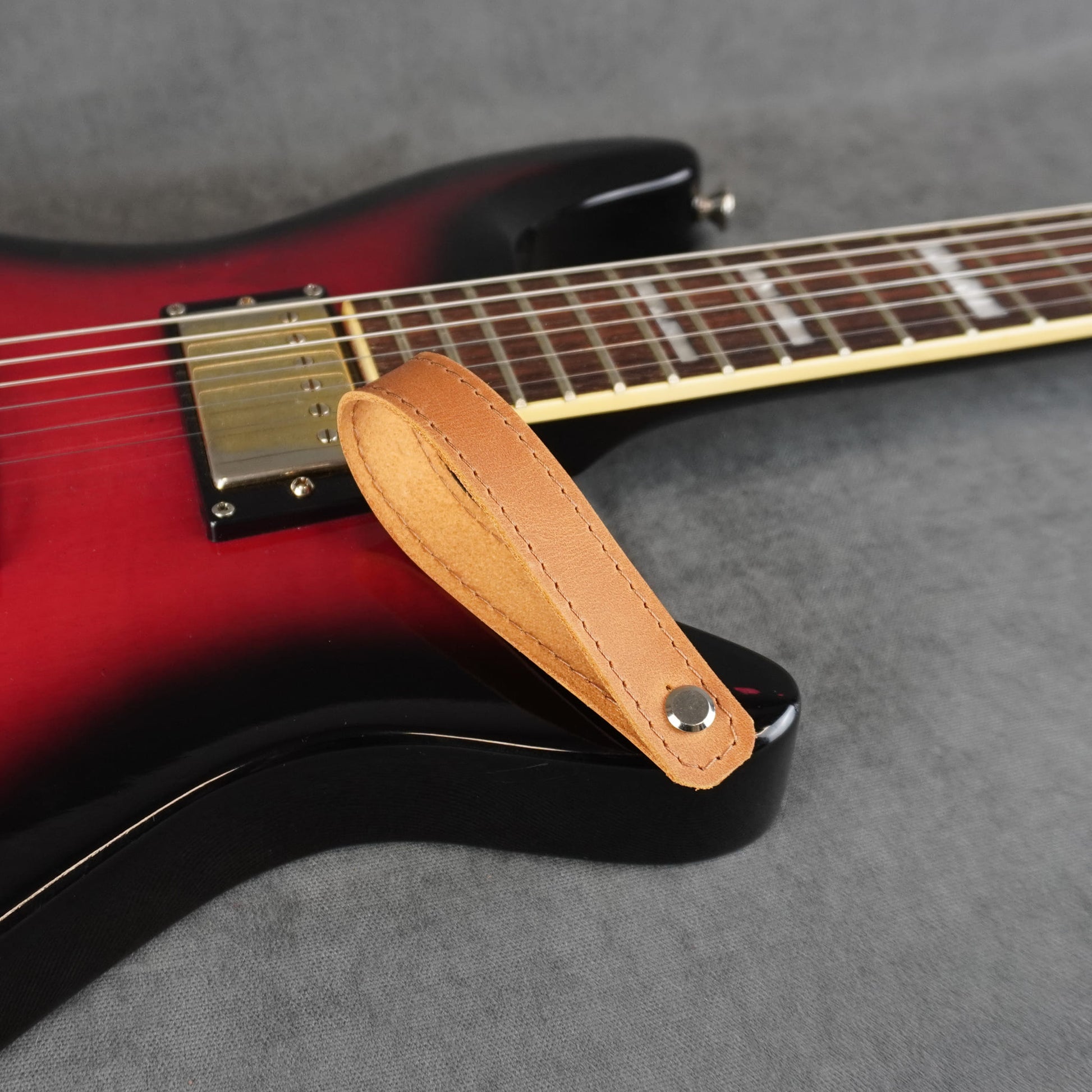 A close-up of an electric guitar with a tan leather guitar headstock adapter