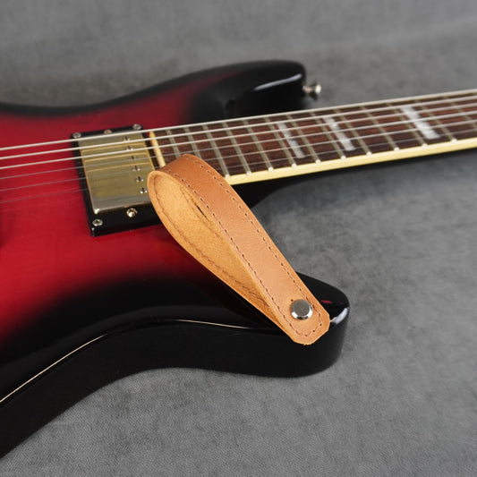 A close-up of an electric guitar with a tan leather guitar headstock adapter