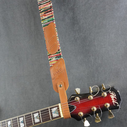 A guitar strap with a colorful striped fabric with tan leather headstock adapter