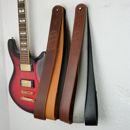 Guitar straps in brown, tan, black, and gray hanging on a white wall next to a red electric guitar.