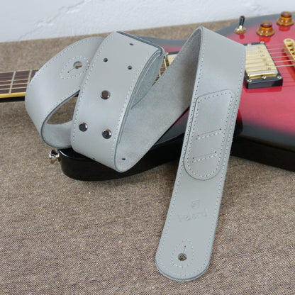 A light gray guitar strap with metal rivets and a stitched end tab, draped over a red electric guitar on a textured gray surface.