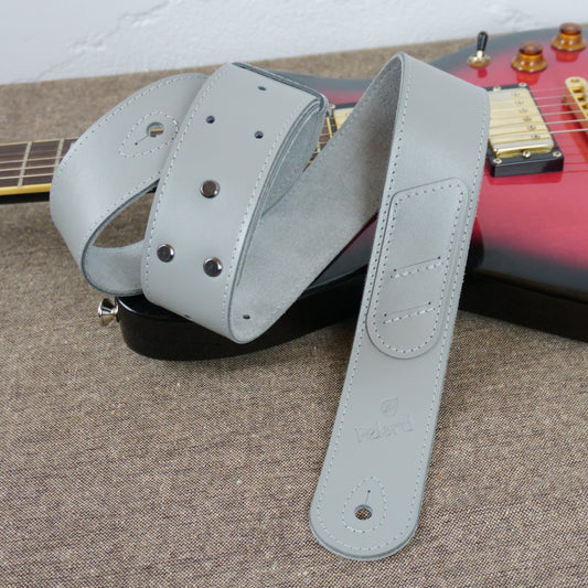 A light gray guitar strap with metal rivets and a stitched end tab, draped over a red electric guitar on a textured gray surface.