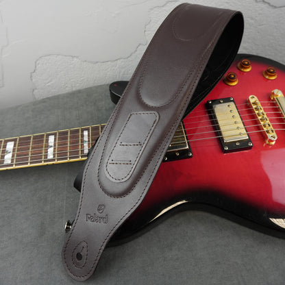 A dark brown leather guitar strap with the brand name 'Felard' embossed on it, draped over a red electric guitar on a gray surface.