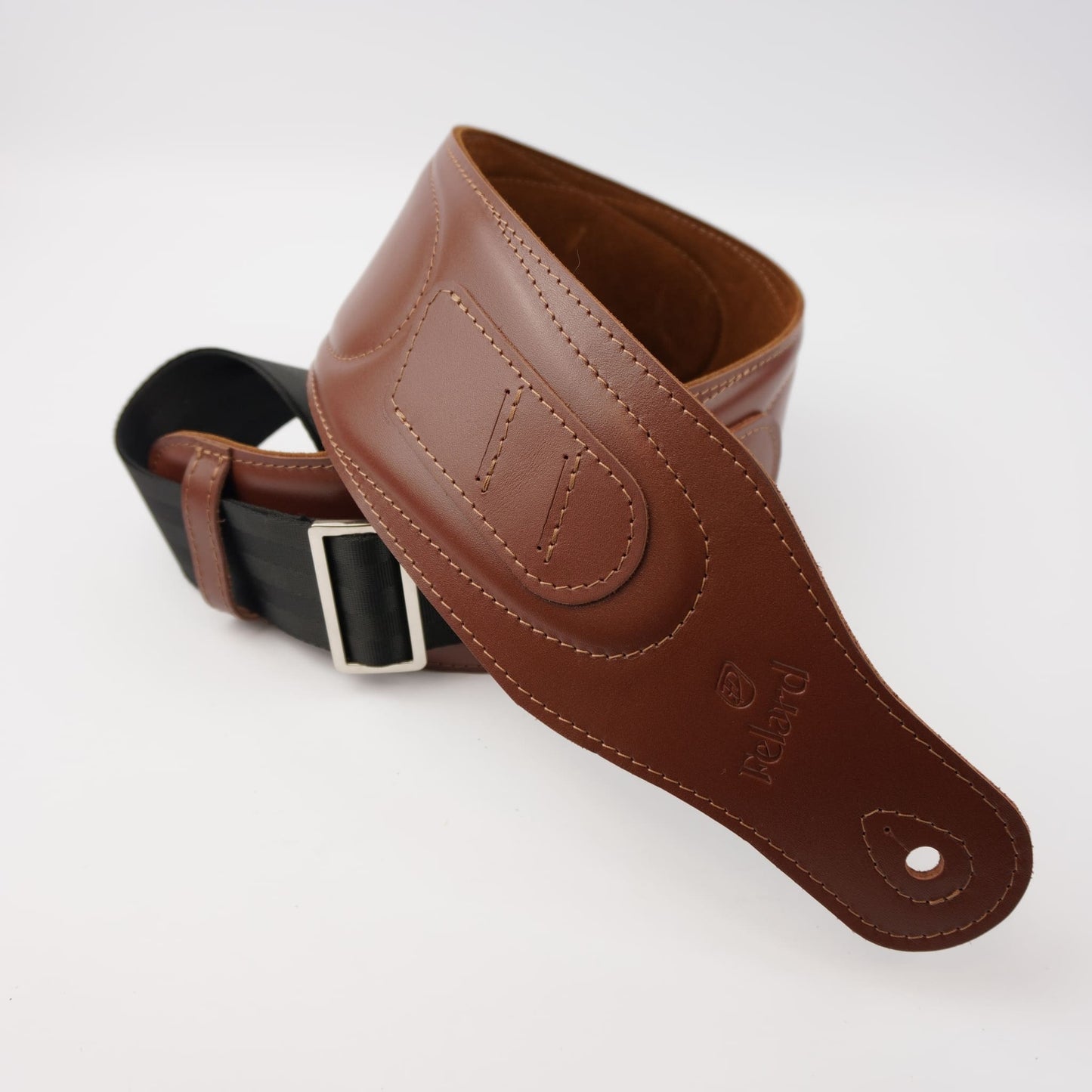 A brown leather guitar strap with a silver buckle, shown coiled on a white background. 