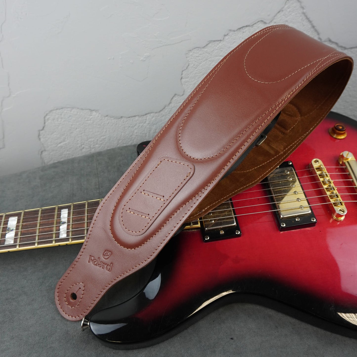 A brown leather electric guitar strap with visible 'Felard' branding