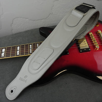 A light gray padded electric guitar strap with a black webbing, laid diagonally across a red electric guitar on a gray surface.