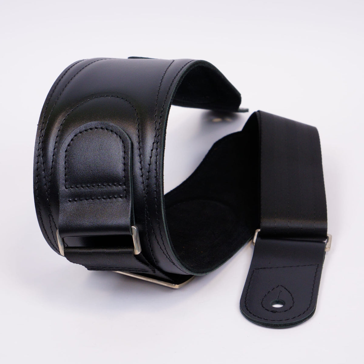 A black leather guitar strap with silver metal hardware, shown coiled on a white background.