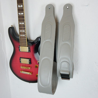 A pair of light gray guitar straps hanging on a white wall next to a red-to-black gradient electric guitar.