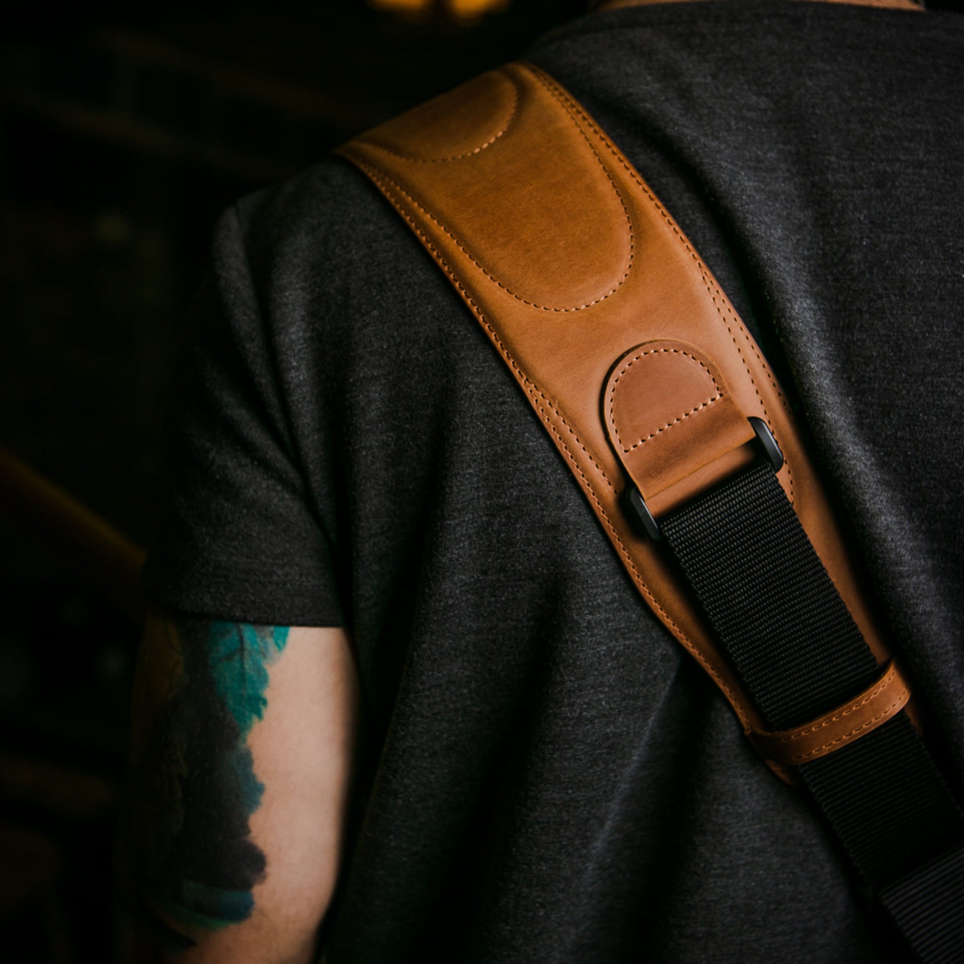 A close-up of a person showing a tan leather guitar strap with a black webbing strap across his shoulder.