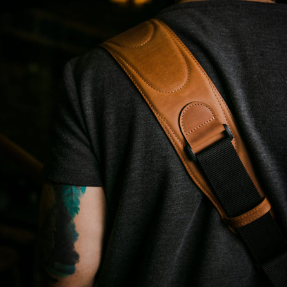 A close-up of a person showing a tan leather guitar strap with a black webbing strap across his shoulder.