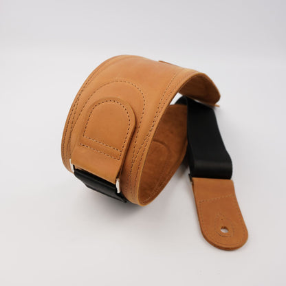 A tan leather guitar strap with a black webbing section and silver metal adjusters, photographed on a light gray background.