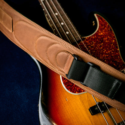 A close-up of a tan leather guitar strap with a black webbing section